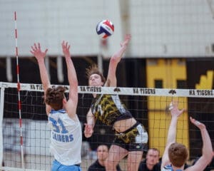 High school volleyball game action; player spikes ball over the net while opposing team attempts to block.