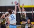High school volleyball players jump to block an opponent's spike at a competitive match. Action-packed scene at the net.