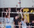 High school volleyball match action, player spiking the ball over the net while defenders jump to block.