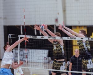 Volleyball players jumping to block a spike at a competitive match, showcasing athletic skill and teamwork.