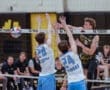 Action shot of a volleyball match with players from two teams blocking and spiking at the net in a competitive setting.
