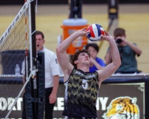 High school volleyball player sets the ball during a competitive match, focused on teamwork and strategy.