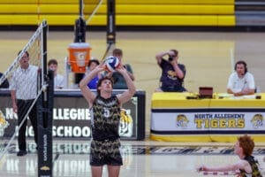 A North Allegheny volleyball player sets the ball as spectators and announcers watch during a high school match.