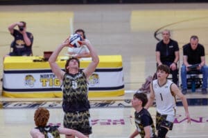 Player prepares to set a volleyball during a high school match, with teammates and coaches in the background.