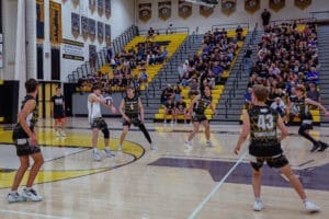 High school boys' volleyball match in gym; players in action with engaged crowd in the stands.