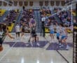 High school boys' volleyball match in action, with players jumping and a packed crowd cheering in the background.