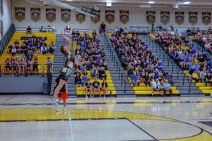 High school volleyball player jumps to spike the ball as a cheering crowd fills the gymnasium.