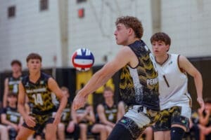 High school volleyball match action, player prepares to set the ball with teammates in the background, captured indoors.