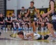 A basketball player dives on the court, while teammates and opponents watch in an intense game moment.