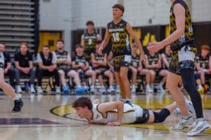 A basketball player dives on the court, while teammates and opponents watch in an intense game moment.