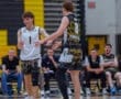 Two young basketball players celebrate on the court after a play, with teammates cheering in the background.