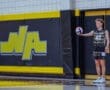 Player in volleyball uniform prepares to serve near the North Allegheny school logo, showcasing athletic spirit and focus.