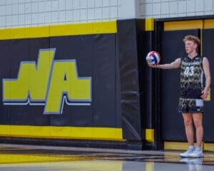 Player in volleyball uniform prepares to serve near the North Allegheny school logo, showcasing athletic spirit and focus.