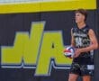 Male volleyball player in North Allegheny uniform preparing to serve, with a vibrant team logo in the background.