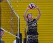 High school volleyball player sets the ball during match, focused on gameplay with teammate in the background.
