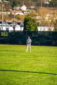A baseball player stands in the outfield on a sunny day, ready for action. Green grass and a fence in the background.