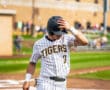 Baseball player in striped uniform adjusts cap and holds bat on field, focused before the game.
