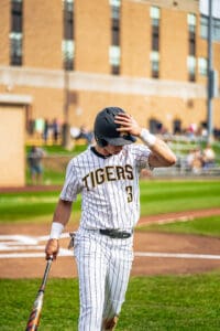 Baseball player in striped uniform adjusts cap and holds bat on field, focused before the game.