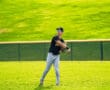 Young baseball player fielding a ball on a green grass field, wearing a black jersey and grey pants, focused and ready.