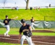 Baseball player in action, fielding the ball on a sunny day, with teammates in the background during a game.