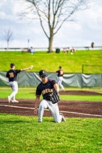Baseball player in action, fielding the ball on a sunny day, with teammates in the background during a game.