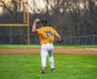 Baseball player in orange jersey throws a ball on a well-maintained field during a game at dusk.