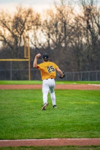 Baseball player in orange jersey throws a ball on a well-maintained field during a game at dusk.