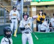 Baseball player in gray uniform prepares to bat while catcher looks on in a lively game environment.