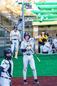 Baseball player in gray uniform prepares to bat while catcher looks on in a lively game environment.