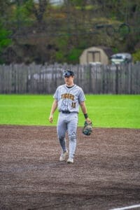 A baseball player in a gray Tigers uniform walks across the field, preparing for the game on a sunny day.
