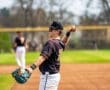 Baseball player in a black jersey throws a ball in a sunny field, showcasing athleticism and team spirit.