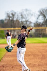 Baseball player in a black jersey throws a ball in a sunny field, showcasing athleticism and team spirit.