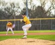 A young baseball pitcher in a bright yellow uniform prepares to pitch on the mound during a game.