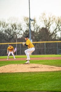 A young baseball pitcher in a bright yellow uniform prepares to pitch on the mound during a game.