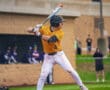 Baseball player in yellow uniform prepares to swing bat at home plate during a game, with audience in the background.