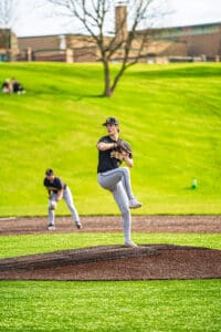 Young baseball player on the pitcher's mound prepares to throw, with teammates in the background and a vibrant green field.