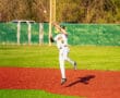 Baseball player leaps to catch a ball during the game on a vibrant red and green field under clear skies.