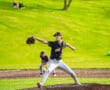 High school baseball pitcher in motion on the mound, with players and greenery in the background.