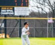 Baseball player in striped uniform running on green field with scoreboard in background showing game stats.