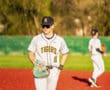 Baseball player in gray Tigers uniform prepares for the game on a vibrant red field with focused expression.