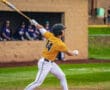 A baseball player in a yellow jersey swings a bat during a game, focused on hitting the ball.