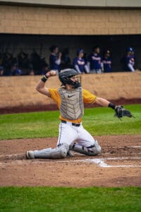Baseball catcher in action, throwing a ball from home plate while wearing a protective gear and focused expression.