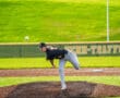 High school baseball player pitching on the mound, with green grass and fences in the background.