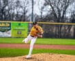A baseball pitcher in a yellow jersey throws a pitch from the mound on a well-maintained field during a game.