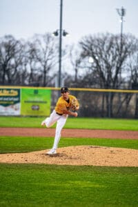 A baseball pitcher in a yellow jersey throws a pitch from the mound on a well-maintained field during a game.