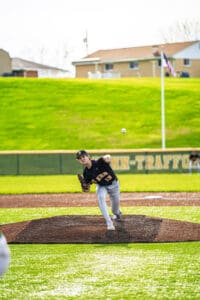 High school baseball pitcher in action, delivering a pitch on a sunny day at the field.