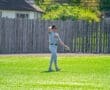 Player in gray baseball uniform stands on a sunny field, preparing for the game, glove in hand, background of trees.
