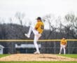 Young baseball pitcher in action on the mound during a game, with teammate in the background on the field.