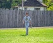 A baseball player walks on a sunny field, wearing a Tigers jersey and preparing for the game.