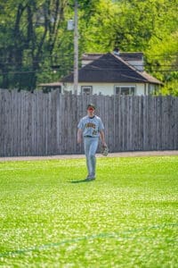 A baseball player walks on a sunny field, wearing a Tigers jersey and preparing for the game.